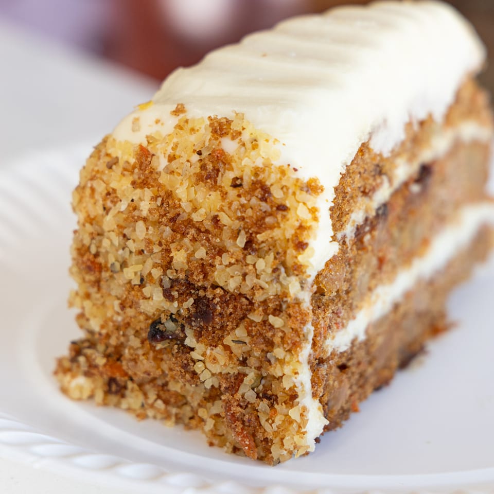 A slice of carrot cake with white cream cheese frosting and a sprinkle of nuts.