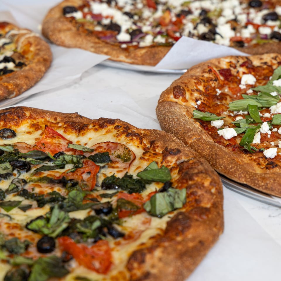 Four delicious Tastivo pizzas with various toppings, including basil, olives, and feta cheese.